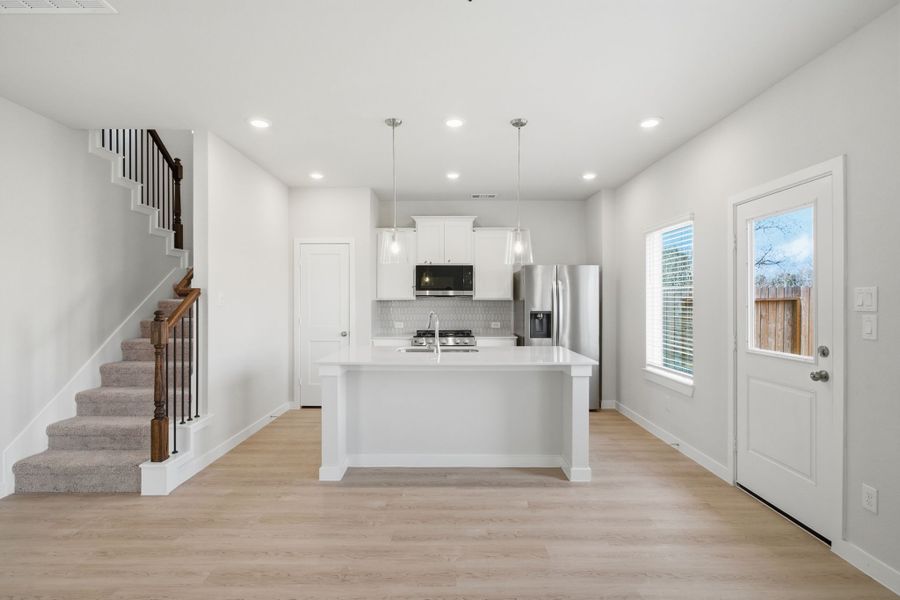 A large kitchen with a large white counter and a white staircase.