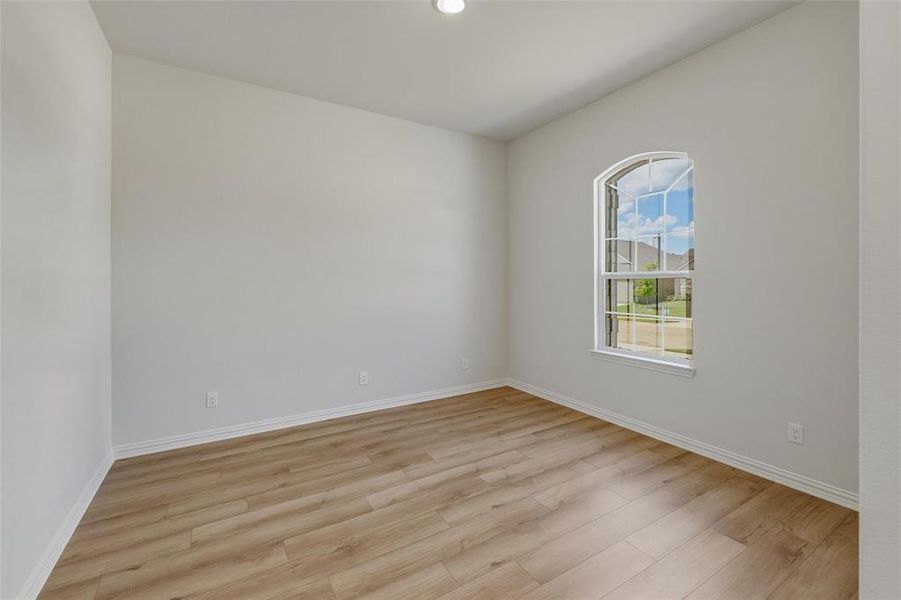 Room featuring light wood-finish flooring, white baseboards, a single arched window with white trim, and a recessed ceiling light fixture Room featuring light wood-finish flooring, white baseboards, a single arched window with white trim, and a recessed ceiling light fixture