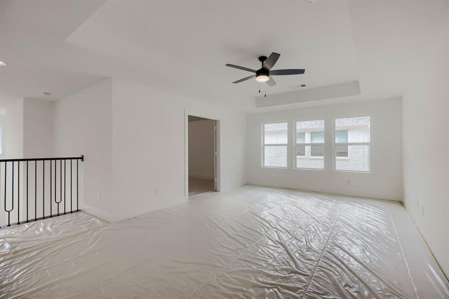 Spacious room featuring a tray ceiling, ceiling fan with integrated lighting, and three large windows Spacious room featuring a tray ceiling, ceiling fan with integrated lighting, and three large windows