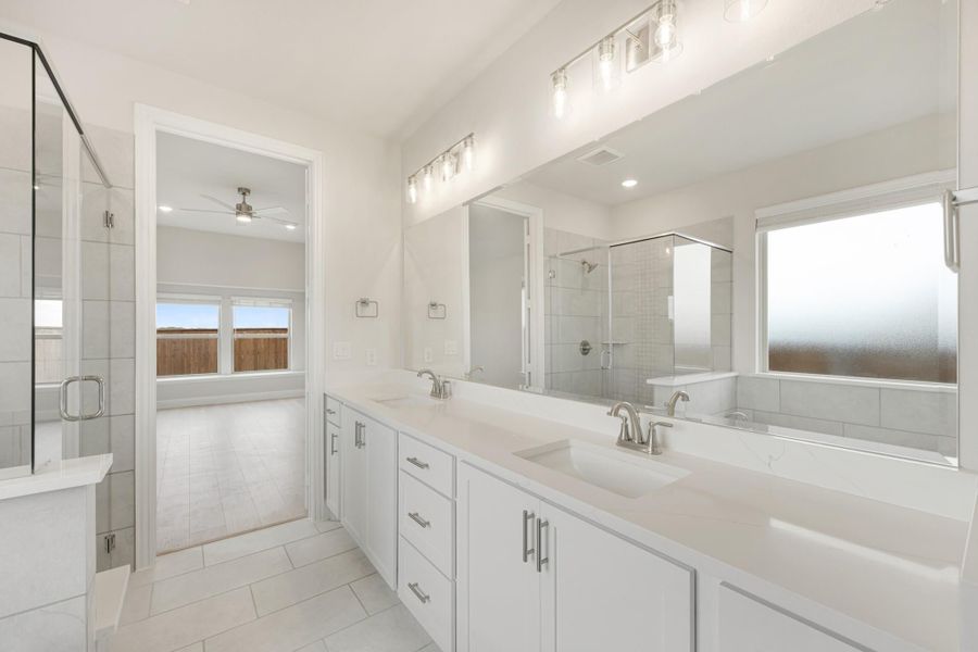 Ensuite bathroom with double vanity, white cabinets, glass shower, and large mirror with overhead lighting
