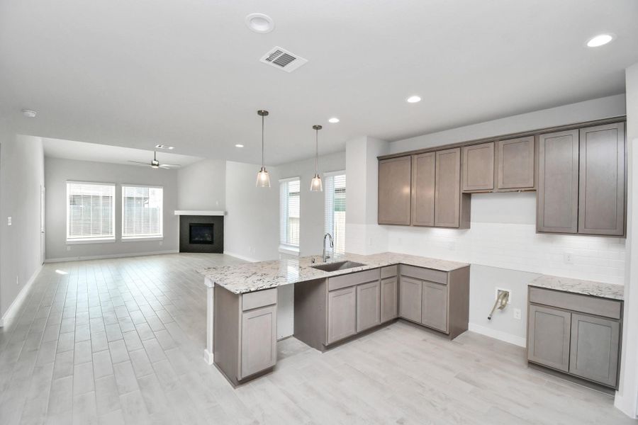 This kitchen is truly a chef's dream! This haven Boasts high ceilings, recessed & pendant lighting, stained wood cabinets, granite countertops, stainless steel appliances, a modern tile backsplash.  All of this overlooks your expansive family room, creating a perfect space for culinary delights and family gatherings. Sample photo of completed home with similar floor plan. Actual colors and selections may vary.