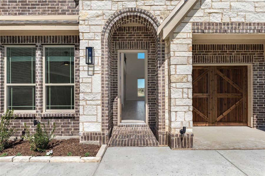 Home entrance with brick arched doorway, stone exterior, and wood barn-style garage door nearby. Home entrance with brick arched doorway, stone exterior, and wood barn-style garage door nearby.