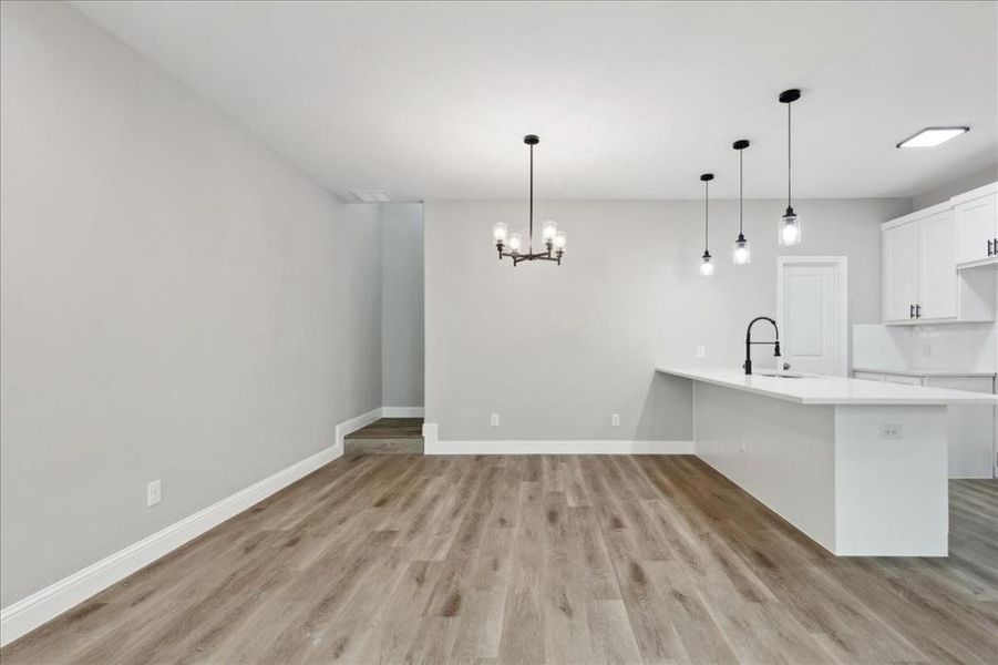 Kitchen featuring white cabinetry, kitchen peninsula, light hardwood / wood-style floors, decorative light fixtures, and sink