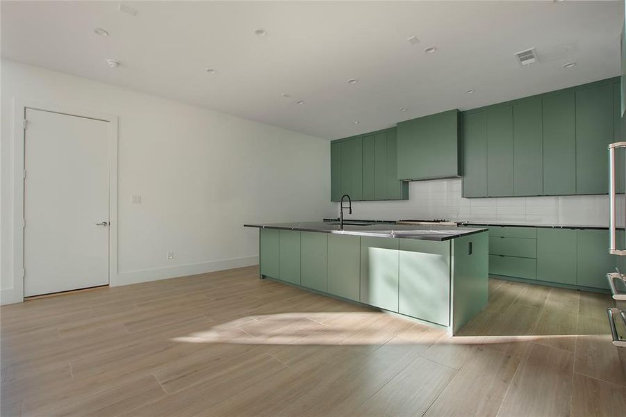 Kitchen with green cabinets, tasteful backsplash, a kitchen island with sink, wall chimney exhaust hood, and sink