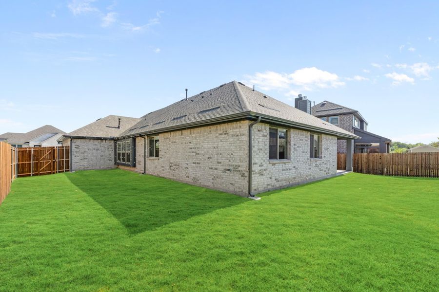 Rear view of single-story brick home with large green lawn and wood privacy fence