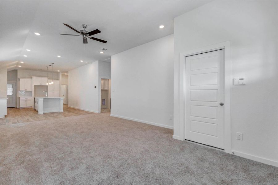 Spacious open living area with soft carpet, high ceilings, recessed lighting, ceiling fan, and direct sightlines into the kitchen and dining area. The open layout creates an easy flow for everyday living, relaxing, and entertaining.