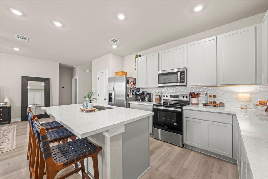 A contemporary kitchen features bright white cabinetry, stainless steel appliances, and a spacious island with seating. A contemporary kitchen features bright white cabinetry, stainless steel appliances, and a spacious island with seating.