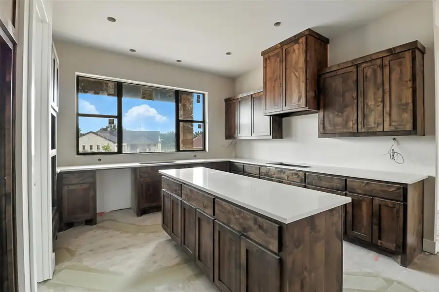 Kitchen with dark brown cabinetry, a kitchen island, recessed lighting, and light stone counters Kitchen with dark brown cabinetry, a kitchen island, recessed lighting, and light stone counters