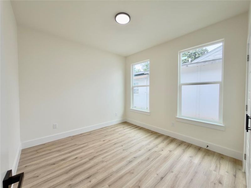 Neutral-toned interior room featuring wood-finish flooring, two large windows, white baseboards, and a ceiling-mounted light fixture