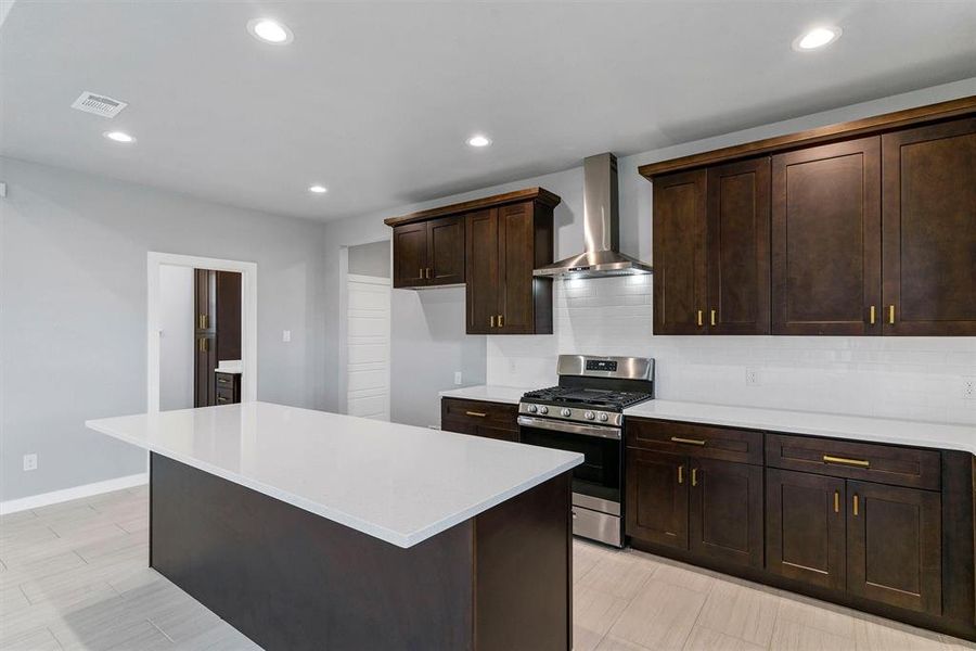 Kitchen with decorative backsplash, dark brown cabinets, wall chimney range hood, a center island, and stainless steel range with gas stovetop