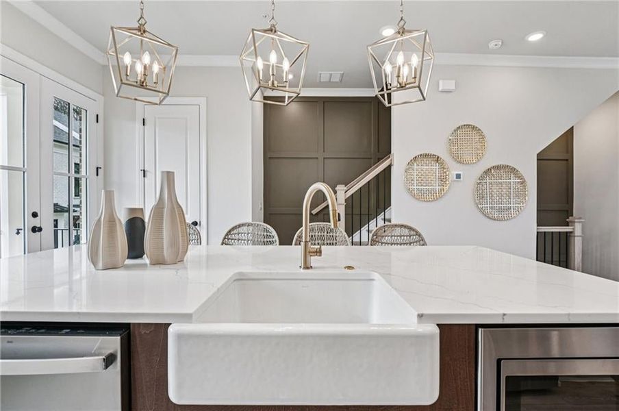 Kitchen with ornamental molding, appliances with stainless steel finishes, dark brown cabinets, light stone countertops, and pendant lighting