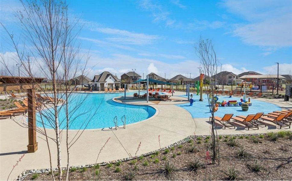 Expansive community pool area featuring a large swimming pool, a dedicated splash pad with water features, a shaded lounging pavilion, and a separate building with a covered patio Expansive community pool area featuring a large swimming pool, a dedicated splash pad with water features, a shaded lounging pavilion, and a separate building with a covered patio