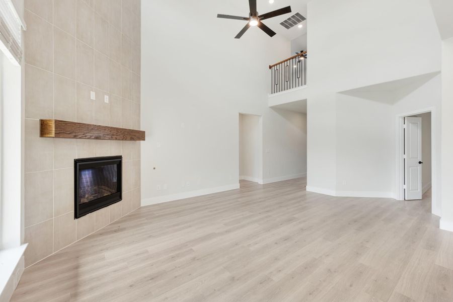 Open living room with vaulted ceiling, tile fireplace, wood mantel, and light hardwood floors