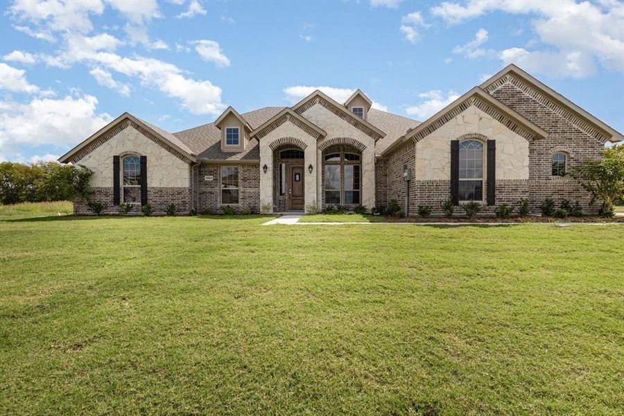 French country inspired facade with stone siding, brick siding, a front lawn, and a shingled roof French country inspired facade with stone siding, brick siding, a front lawn, and a shingled roof