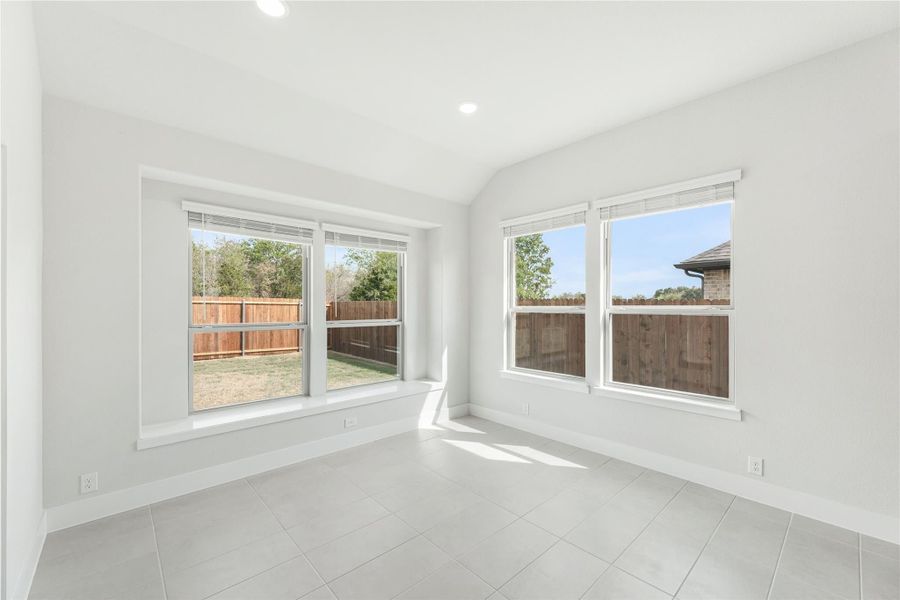 Bright empty room with tile floors, white walls, and large windows overlooking a fenced backyard
