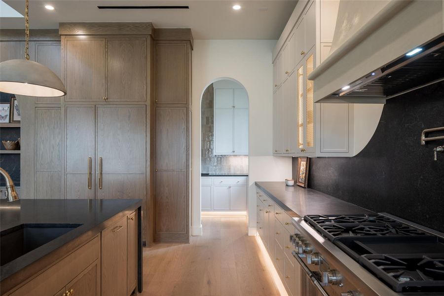 This view captures the kitchen’s layered elegance—anchored by a hidden custom-paneled Thermador refrigerator that blends seamlessly into the surrounding white oak cabinetry. Soft archways lead into the adjacent butlers pantry, while curved elements like the plastered vent hood and sculpted stone backsplash reinforce the home’s signature design language with Thermador range. This view captures the kitchen’s layered elegance—anchored by a hidden custom-paneled Thermador refrigerator that blends seamlessly into the surrounding white oak cabinetry. Soft archways lead into the adjacent butlers pantry, while curved elements like the plastered vent hood and sculpted stone backsplash reinforce the home’s signature design language with Thermador range.