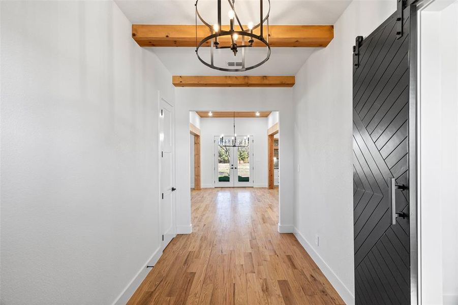 Corridor with french doors, beam ceiling, a barn door, a chandelier, and light hardwood / wood-style floors