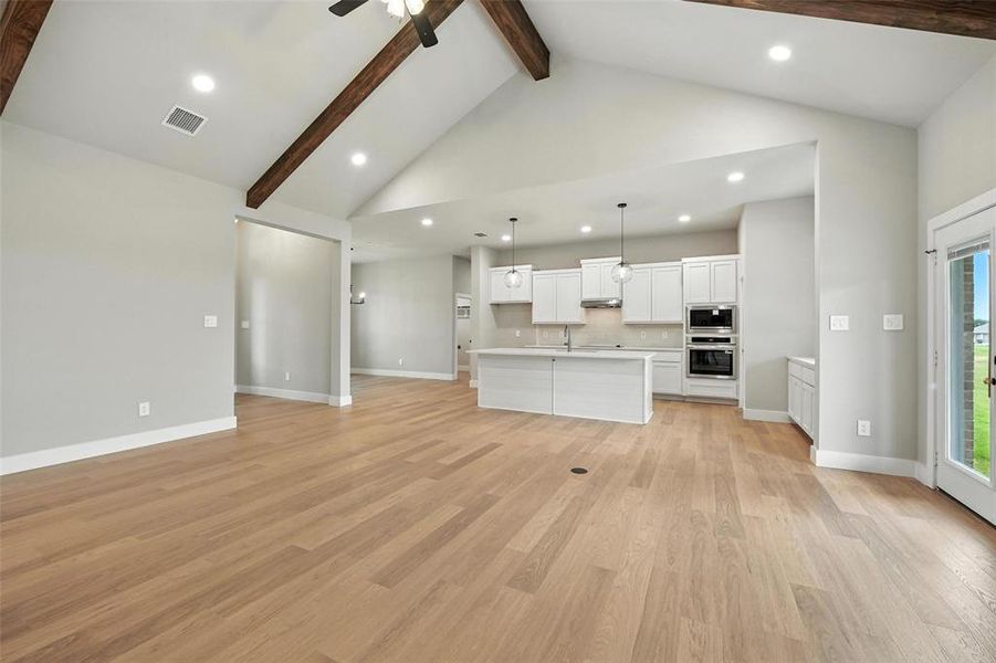 Unfurnished living room with beamed ceiling, a ceiling fan, light wood-style flooring, recessed lighting, and high vaulted ceiling Unfurnished living room with beamed ceiling, a ceiling fan, light wood-style flooring, recessed lighting, and high vaulted ceiling