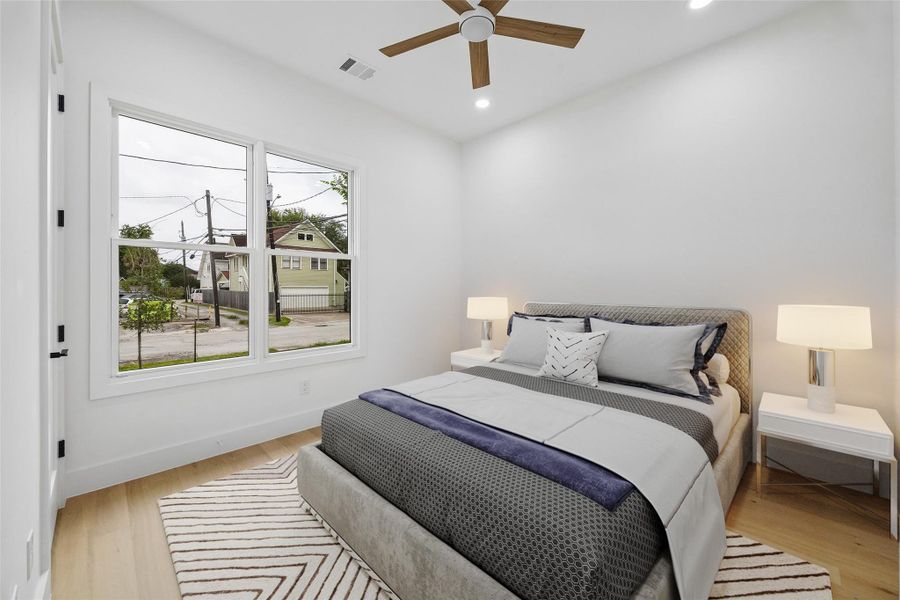 The first floor secondary bedroom offers a bright and flexible layout with oversized windows, engineered wood flooring, and recessed lighting throughout. Positioned near the upper-level living spaces, the room was designed to function comfortably for guests, family, or future office use while maintaining the home’s clean architectural aesthetic. (digitally staged)