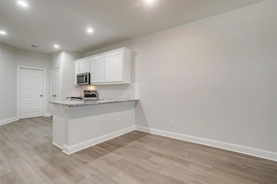 Kitchen featuring white cabinetry, decorative backsplash, light stone countertops, light wood-style floors, and a peninsula