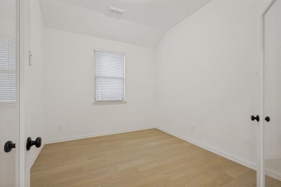Bright interior space featuring light wood-finish flooring, white walls, and a window with blinds