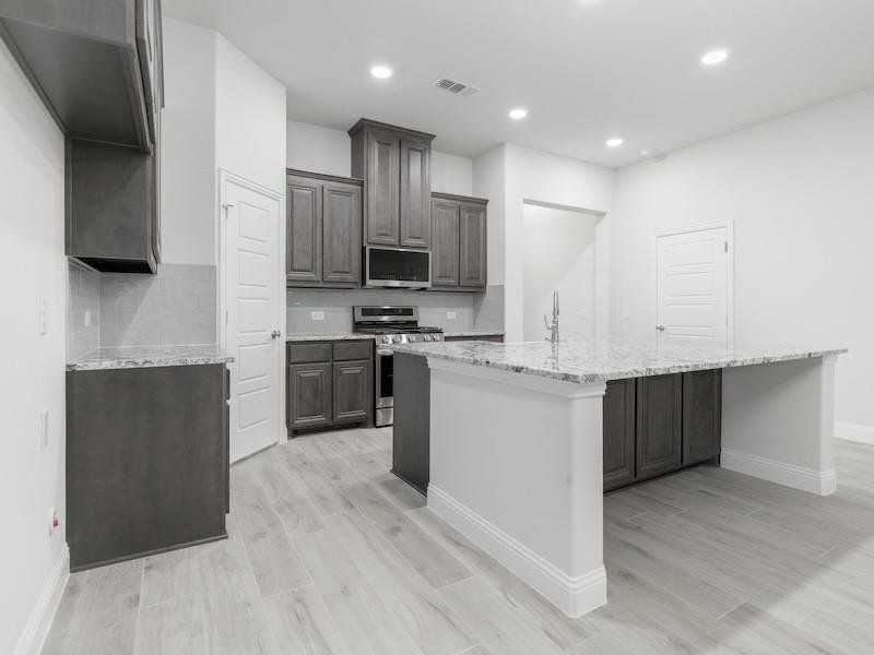 Kitchen with a kitchen island with sink, decorative backsplash, light wood-type flooring, and appliances with stainless steel finishes