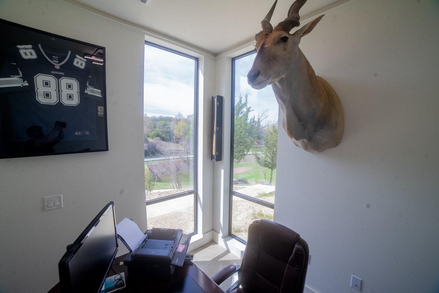This exceptional home office is defined by expansive corner windows that offer panoramic scenic views and a constant stream of natural light. Blending professional functionality with distinctive personality, the room features ample space for high-tech office equipment alongside unique design touches like a framed jersey and an animal mount, creating a sophisticated yet personal retreat