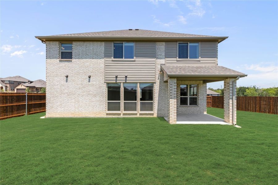 Two-story brick home rear view with covered patio, large windows, and fenced backyard with green lawn