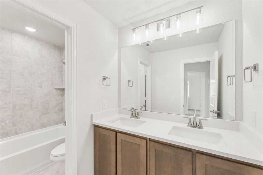 Bathroom with double sink vanity, wood cabinets, large mirror, and tiled tub-shower combo