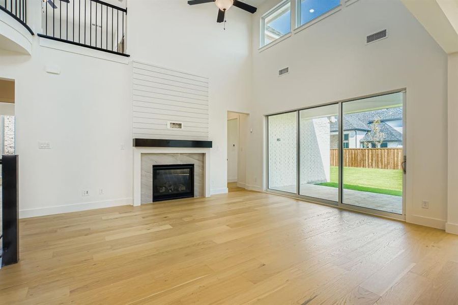 Unfurnished living room with a ceiling fan, light wood-style flooring, a fireplace, and a high ceiling Unfurnished living room with a ceiling fan, light wood-style flooring, a fireplace, and a high ceiling