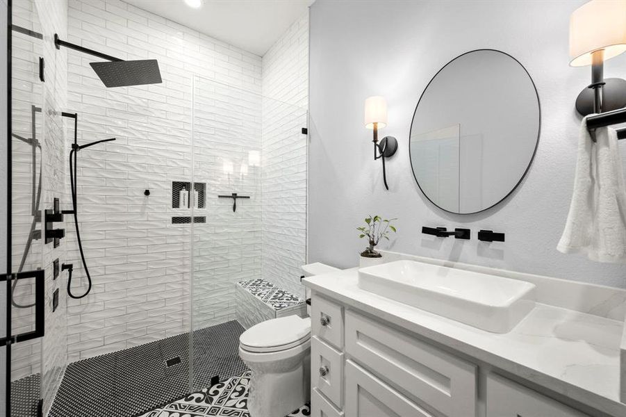 Secondary bath with floor to ceiling tile in walk-in shower featuring a jet system, handheld showerhead, rain head, bench, and European glass. Wall mounted faucet and controls over flat vessel sink in the gentleman's height vanity with soft-close drawers and doors as well as a comfort height toilet with soft-close lid