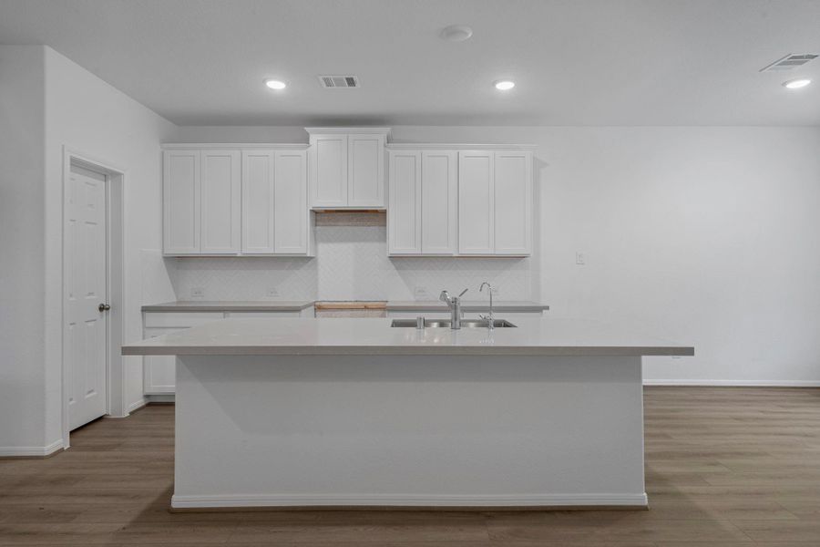 This light and bright kitchen features a large quartz island, white cabinets, a large sink overlooking your family room, recessed lighting, and beautiful backsplash. This light and bright kitchen features a large quartz island, white cabinets, a large sink overlooking your family room, recessed lighting, and beautiful backsplash.