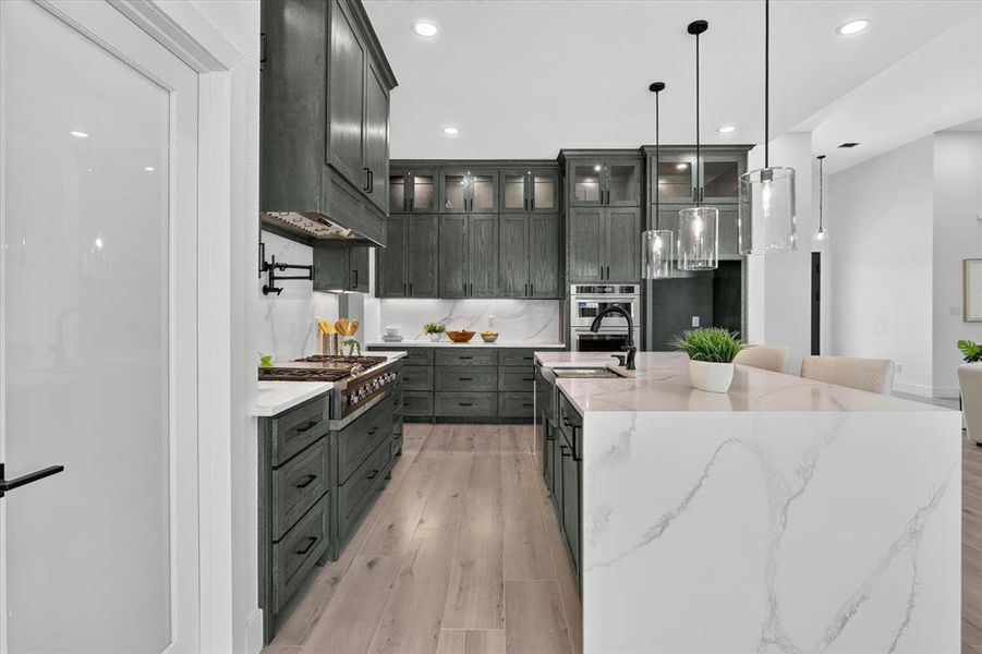 Gourmet kitchen featuring a waterfall island with stone countertop, dark wood-finish cabinetry, stainless steel appliances, and pendant lighting