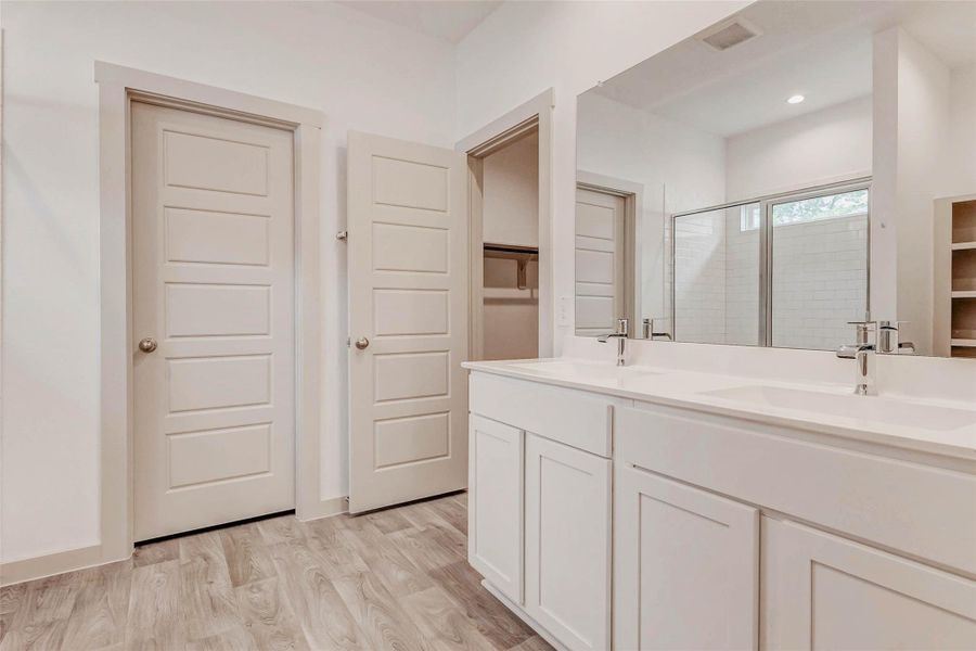 Bright, clean, and beautifully finished, this primary bath features double vanities with sleek fixtures, a full-width mirror, and a spacious glass-enclosed shower with classic subway tile. Neutral tones and wood-look floors add warmth to the fresh, modern aesthetic. Bright, clean, and beautifully finished, this primary bath features double vanities with sleek fixtures, a full-width mirror, and a spacious glass-enclosed shower with classic subway tile. Neutral tones and wood-look floors add warmth to the fresh, modern aesthetic.