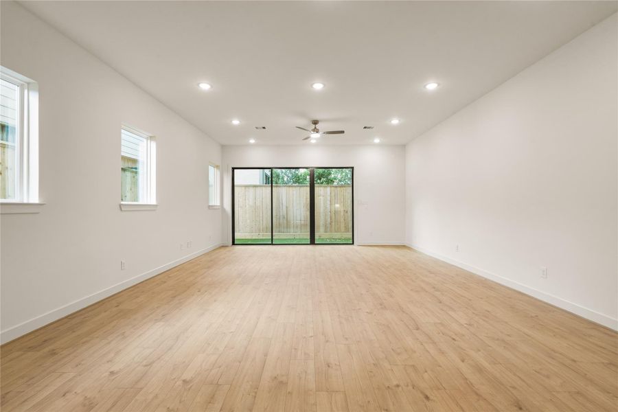 Spacious main living hall — wall-to-wall oak-look flooring, recessed LED lighting throughout, side-yard accent windows, and oversized glass sliding doors opening to the backyard.
