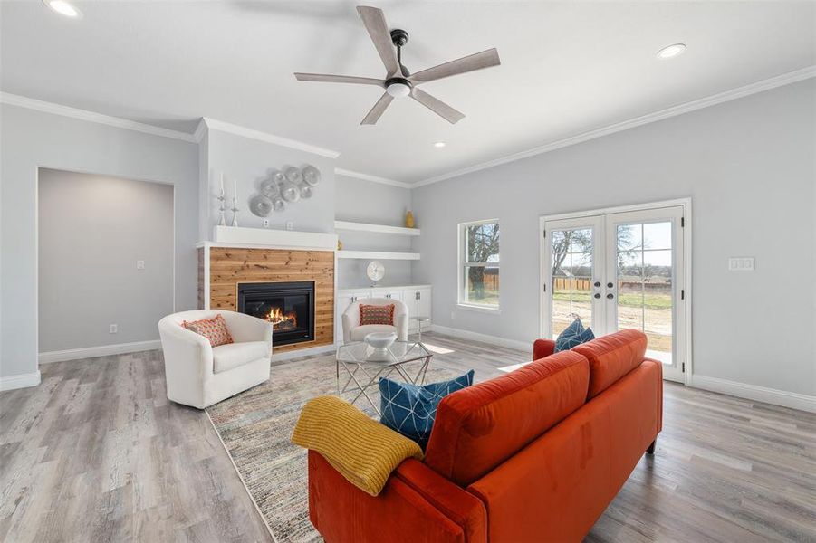 Living room featuring light hardwood / wood-style flooring, ornamental molding, a tiled fireplace, built in shelves, and french doors