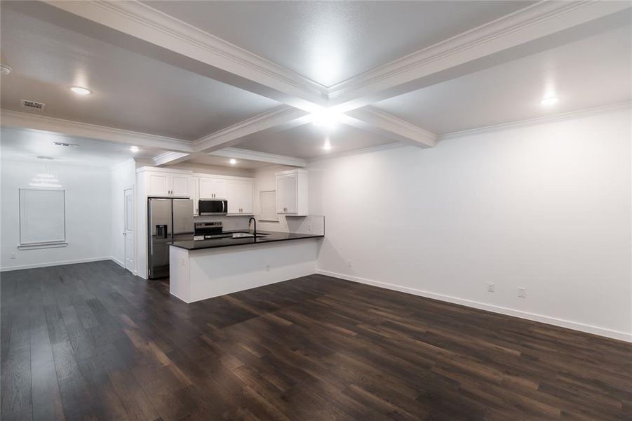 Kitchen featuring dark wood-style floors, crown molding, a peninsula, dark countertops, and appliances with stainless steel finishes Kitchen featuring dark wood-style floors, crown molding, a peninsula, dark countertops, and appliances with stainless steel finishes