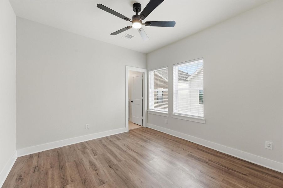 Bright secondary bedroom featuring wide-plank flooring, a modern ceiling fan, and dual windows that bring in abundant natural light.