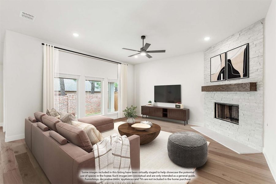 Living room with stone fireplace, hardwood floors, ceiling fan, and large windows overlooking backyard