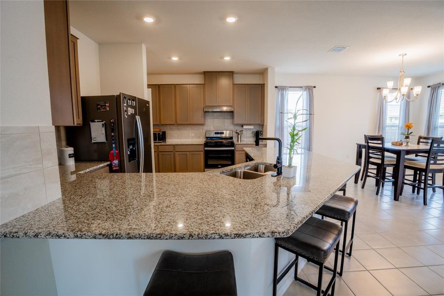 Kitchen featuring granite countertops, a double basin sink with a gooseneck faucet, light wood-finish cabinetry, stainless steel appliances, and recessed lighting Kitchen featuring granite countertops, a double basin sink with a gooseneck faucet, light wood-finish cabinetry, stainless steel appliances, and recessed lighting