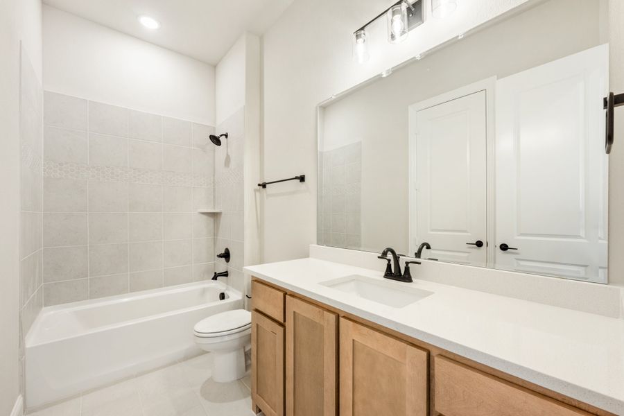 Bathroom with wood vanity, white countertop, tiled tub-shower combo, and black fixtures Bathroom with wood vanity, white countertop, tiled tub-shower combo, and black fixtures