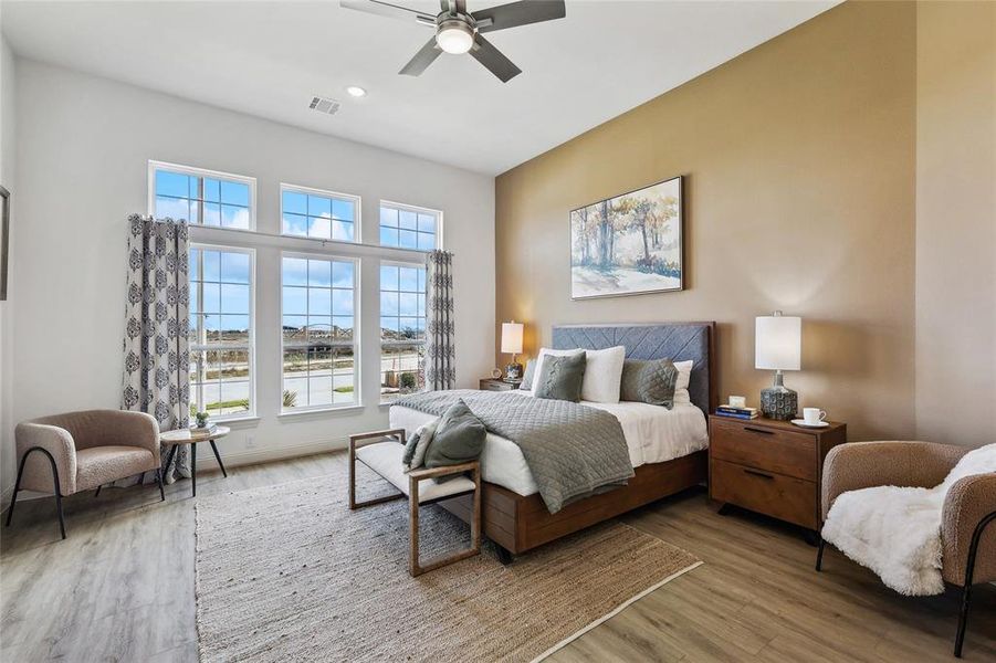 Spacious bedroom featuring multiple large windows, wood-finish flooring, a ceiling fan with integrated lighting, and neutral wall tones