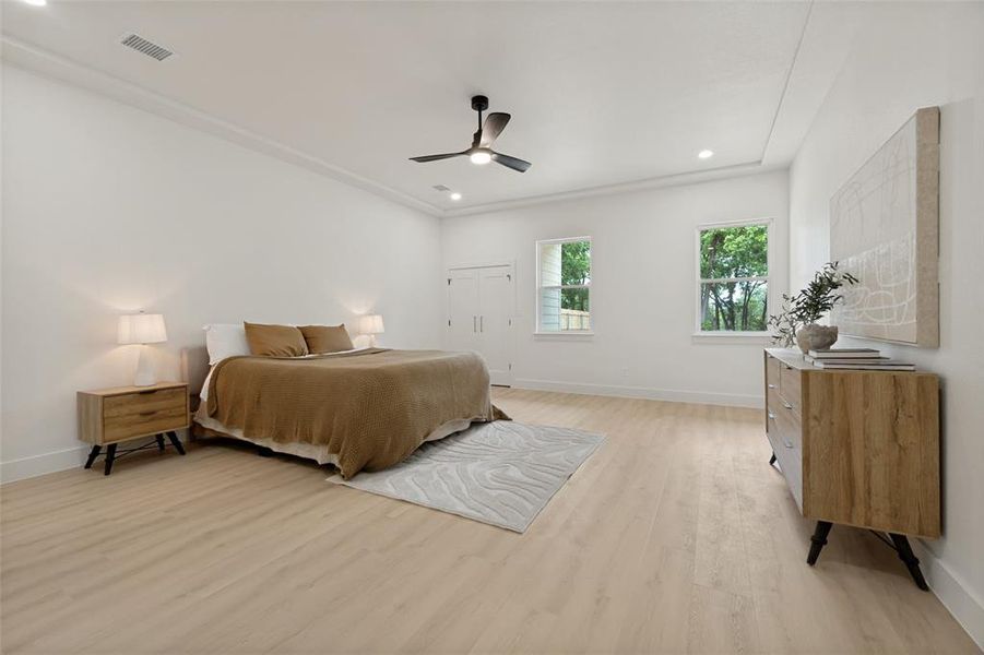 Spacious room featuring light wood-finish flooring, white walls, and a multi-level tray ceiling