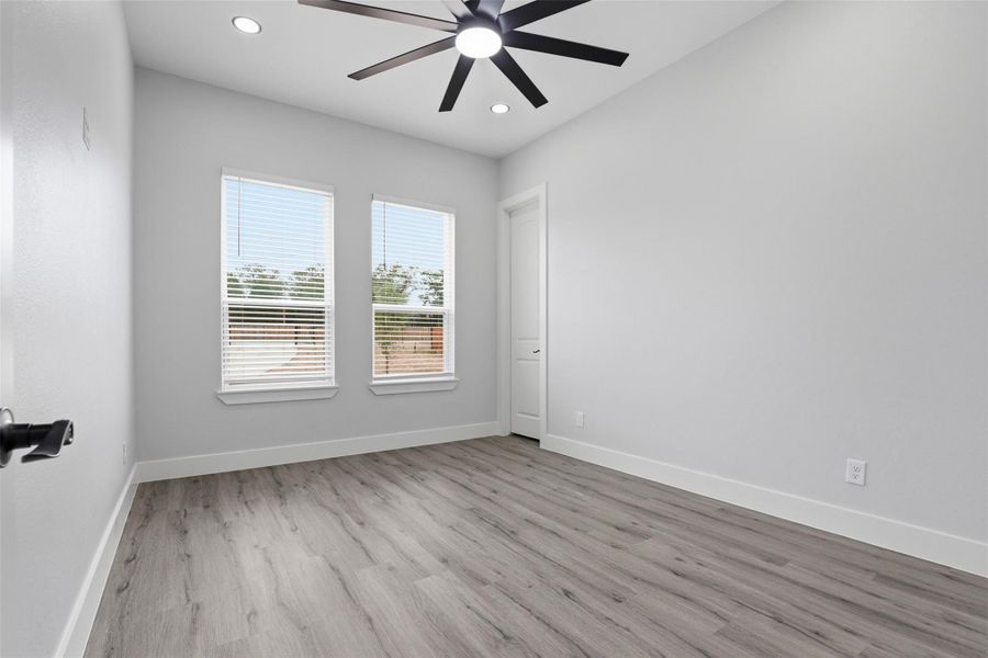 Spacious interior room featuring wood-finish flooring, two windows with blinds, recessed ceiling lights, and a modern ceiling fan