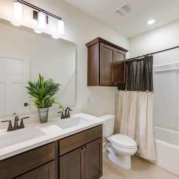 This bathroom features a modern design with a double vanity and dark wood cabinetry. It includes a spacious mirror, elegant lighting, and a combination shower-tub with a stylish curtain. The room is bright and well-lit, creating a fresh and inviting atmosphere.