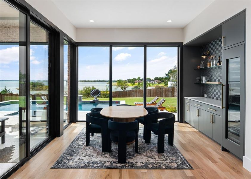 Stunning dining space surrounded by breathtaking lake views, creating a truly unforgettable setting for everyday meals or entertaining. Expansive sliding glass doors fill the room with natural light, while the built-in bar with custom cabinetry and wine storage adds both style and convenience.