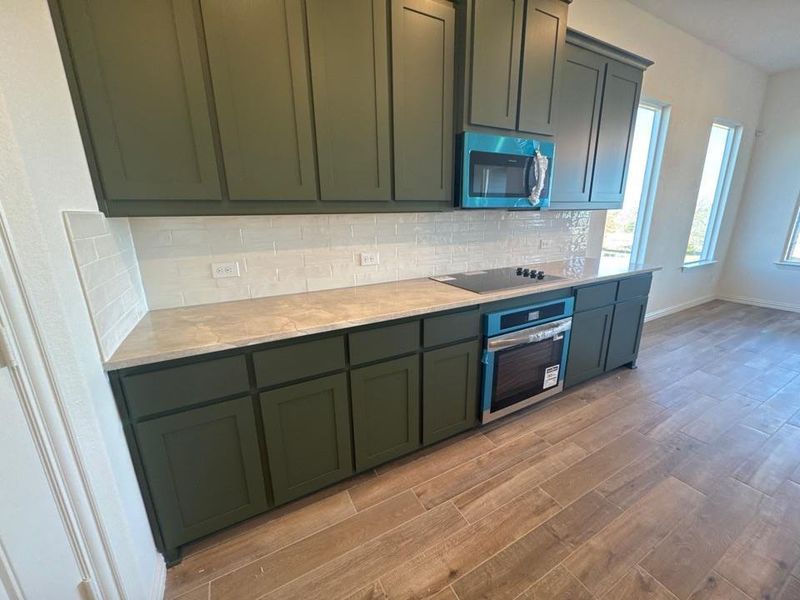 Kitchen featuring stainless steel appliances, wood tiled floors, tasteful backsplash, green cabinets, and light stone counters Kitchen featuring stainless steel appliances, wood tiled floors, tasteful backsplash, green cabinets, and light stone counters