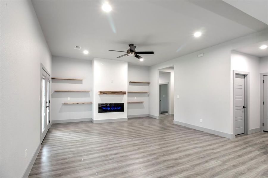 Unfurnished living room featuring light wood finished floors, recessed lighting, ceiling fan, and a glass covered fireplace Unfurnished living room featuring light wood finished floors, recessed lighting, ceiling fan, and a glass covered fireplace