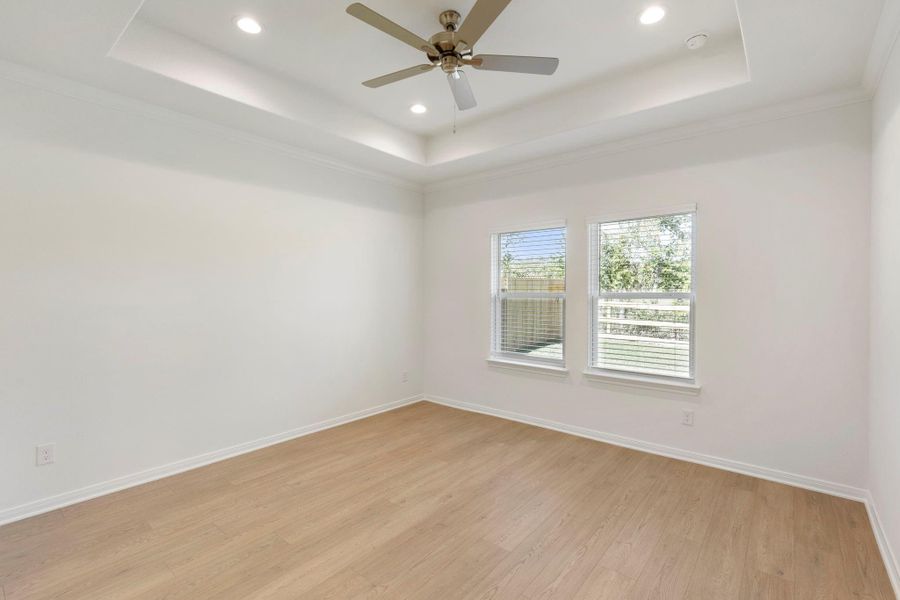 A spacious primary bedroom with a tray ceiling, ceiling fan, and recessed lighting combines comfort and style.