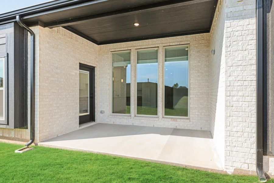 Covered back patio with concrete slab, light brick exterior, and large windows on new home